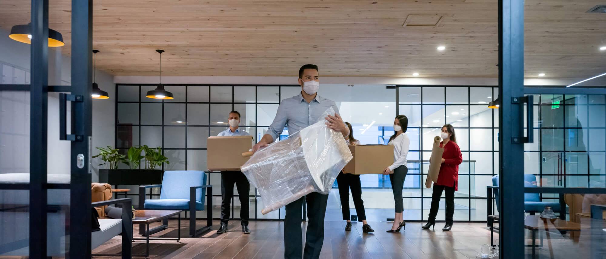 Des salariés en entreprise masqués portant des cartons de déménagement